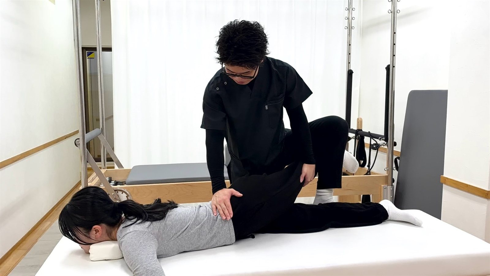 黒いウェアの理学療法士が、うつ伏せのお客様の腰に手を当てて整体をしている様子